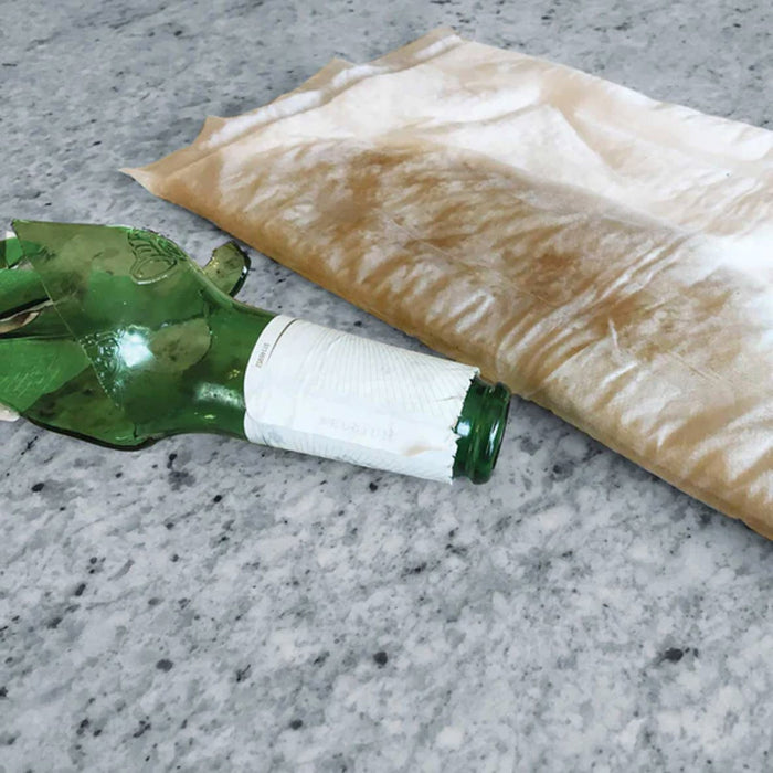 A soaked mat lays on the floor, absorbing the liquid with a broken glass bottle laying next to it - Consolidated Containment