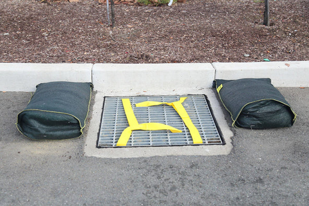 A grate with a Spill Bully's Hornet's Nest and two flood bags on either side of the grate
