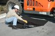 A man bending down to place a black absorbent tarp under a construction vehicle